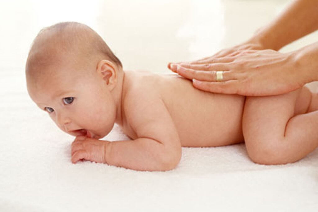 zmẹ đặt bé nằm sấp hoặc ngồi tư thế thẳng, dùng hai tay xoa nhẹ sống lưng theo đường tròn